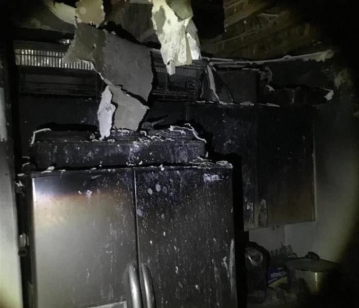 black soot covering kitchen walls, fridge, cabinets and ceiling. Burnt ceiling fallen through and torn.